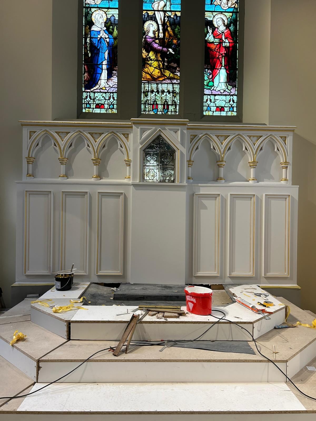 Church altar screen mid-restoration beneath stained glass windows